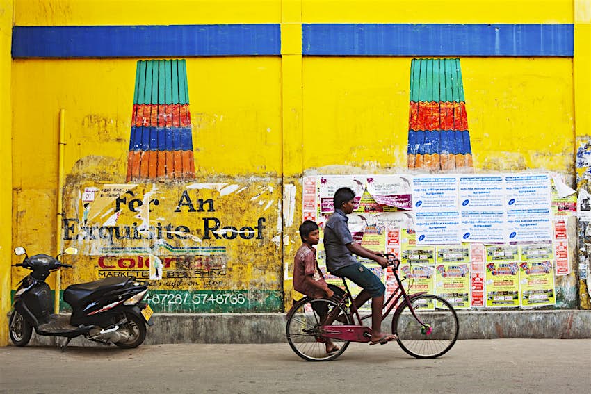 Two young boys ride a bike along a street in Jaffna, Sri Lanka. The one boy sits on the seat and pedals, while the other sits above the back wheel.