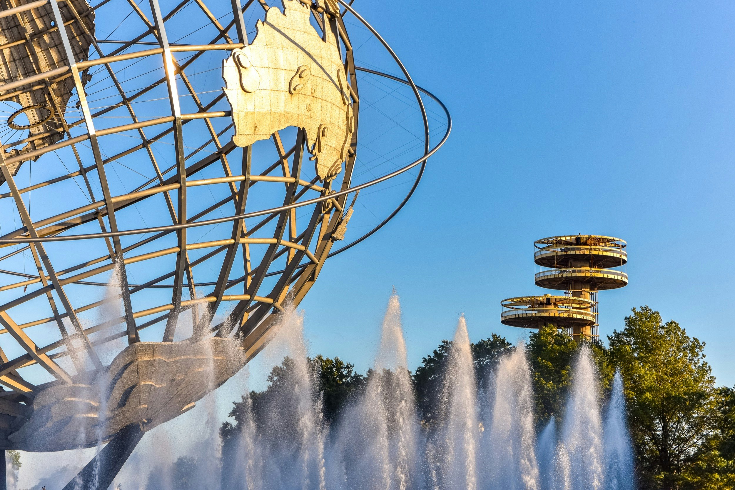 View of part of the wire globe and in the background the structures from the 1939 World's Fair hover above trees.