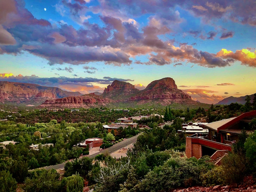 The painted sky of Sedona Arizona in the fall as the sun drops below the desert horizon makes for a stunning backdrop for contemporary homes perched on hills of green.