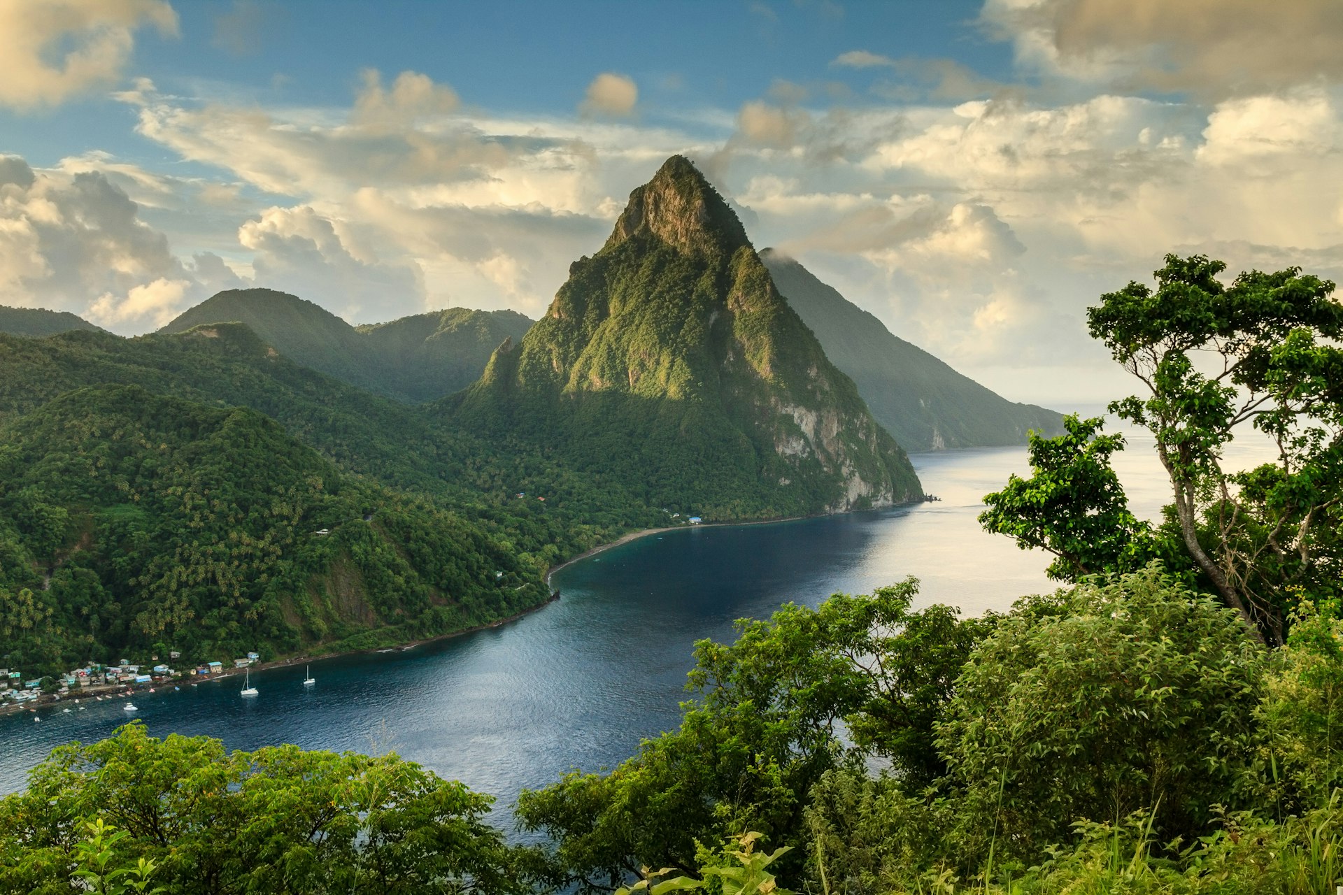 View of St. Lucia's Pitons (Petit Piton & Gros Piton) from an elevated viewpoint with the lush green rainforest and deep blue bay of Soufrière in the foreground. 