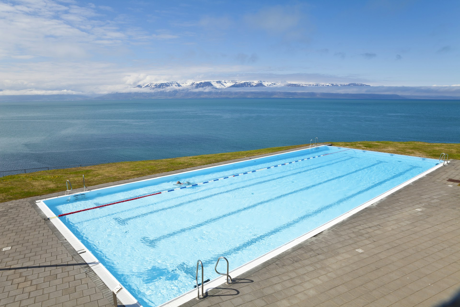 A bright-blue swimming pool on the edge of the sea, providing an infinity pool vibe
