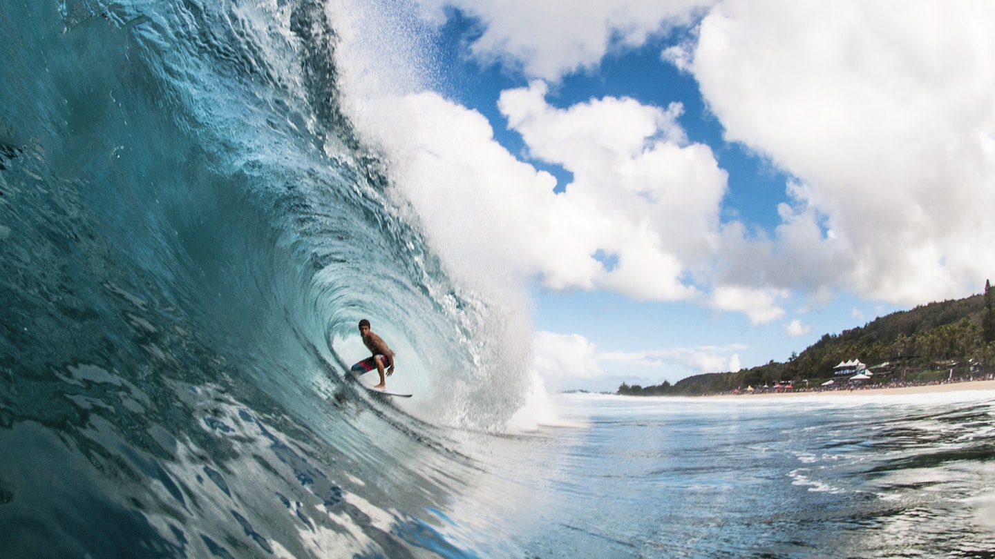 A professional surfer rides through a perfectly blue North Shore barrel