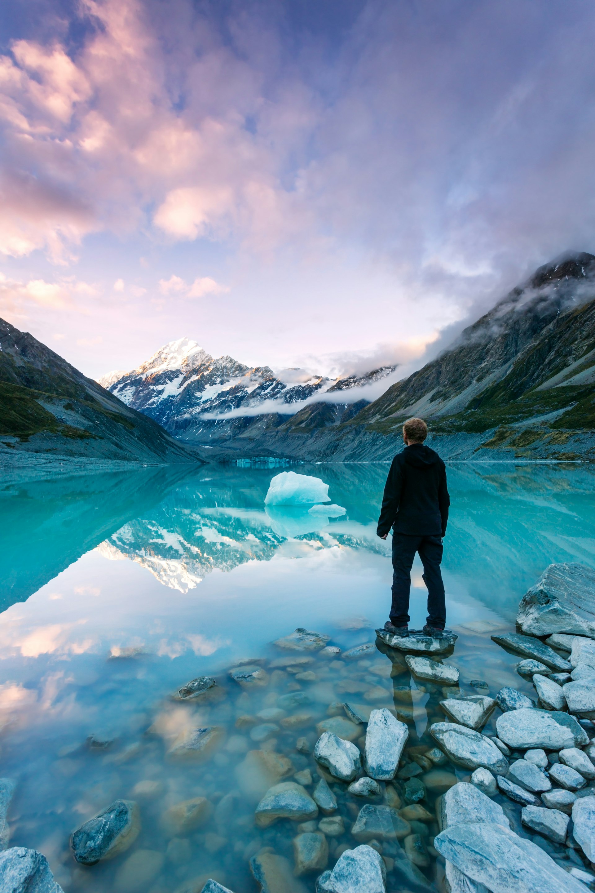 Hiker looks at Mt Cook from a crystal clear lake with an iceberg in New Zealand