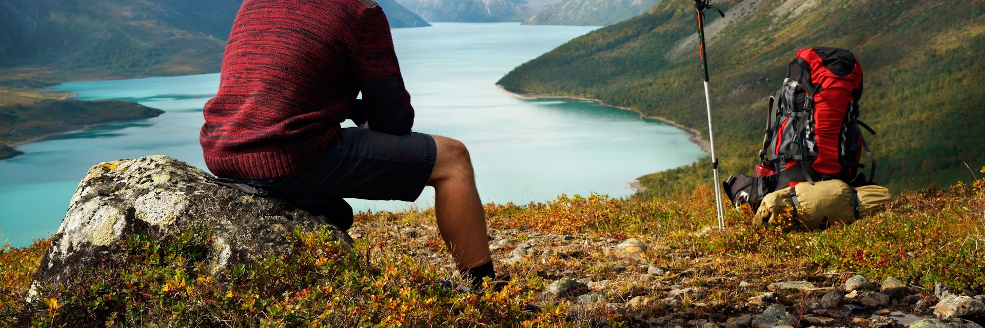 Hiker sitting on a rock in front of Gjendesee Lake in Jotunheimen National Park.
