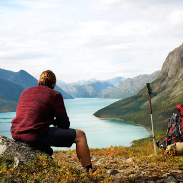 Hiker sitting on a rock in front of Gjendesee Lake in Jotunheimen National Park.
