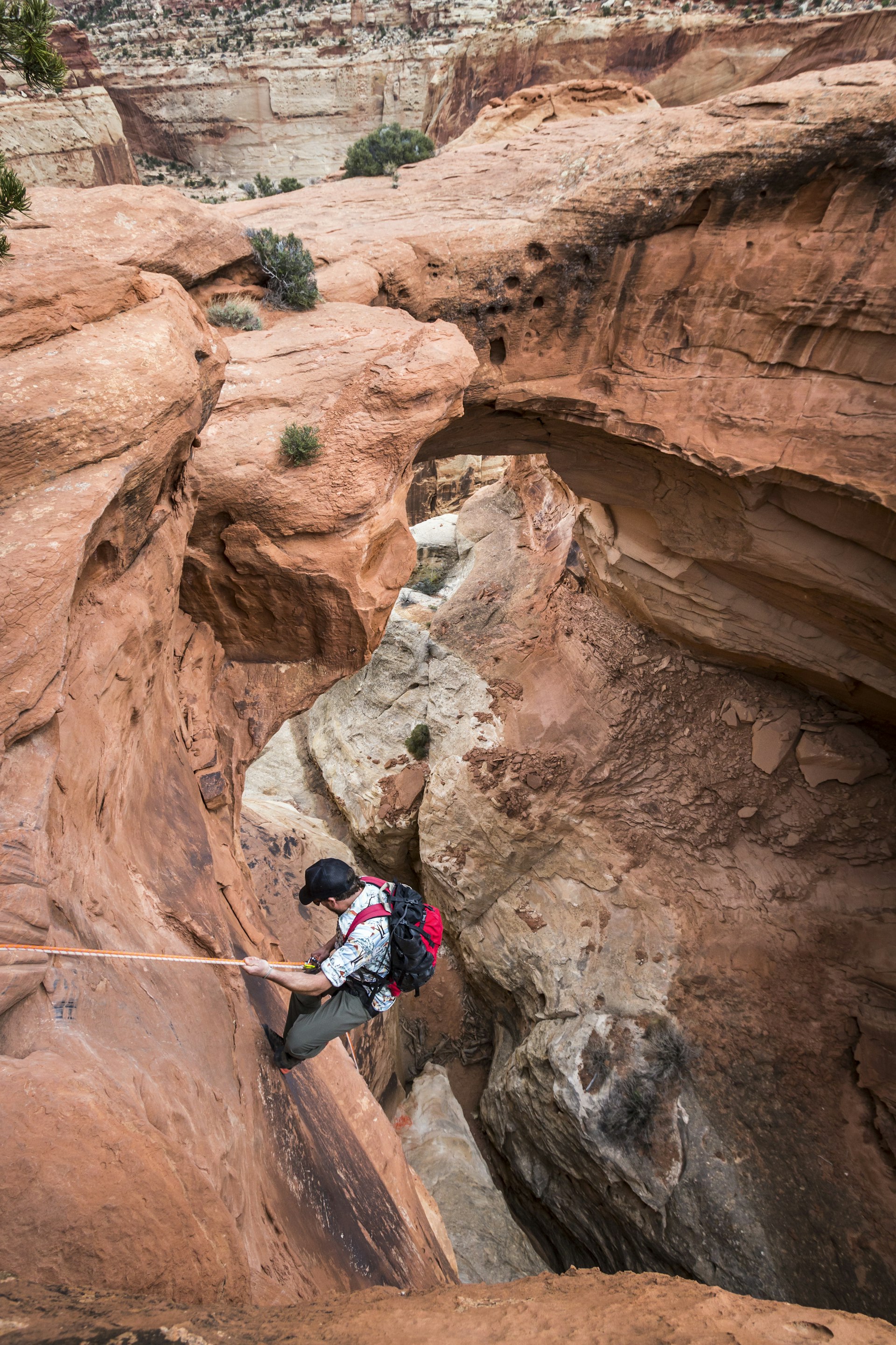 A man rappels down into a canyon below a natural rock arch in the desert