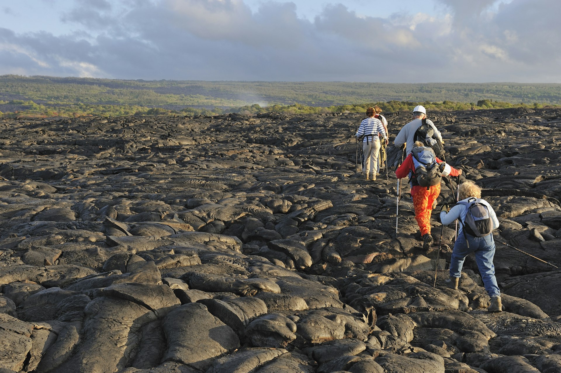 Group of hikers walking on cooled lava flow in Hawaii. 