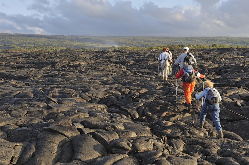 Group of hikers walking on cooled pahoehoe lava flow at sunrise on Kilauea Volcano.