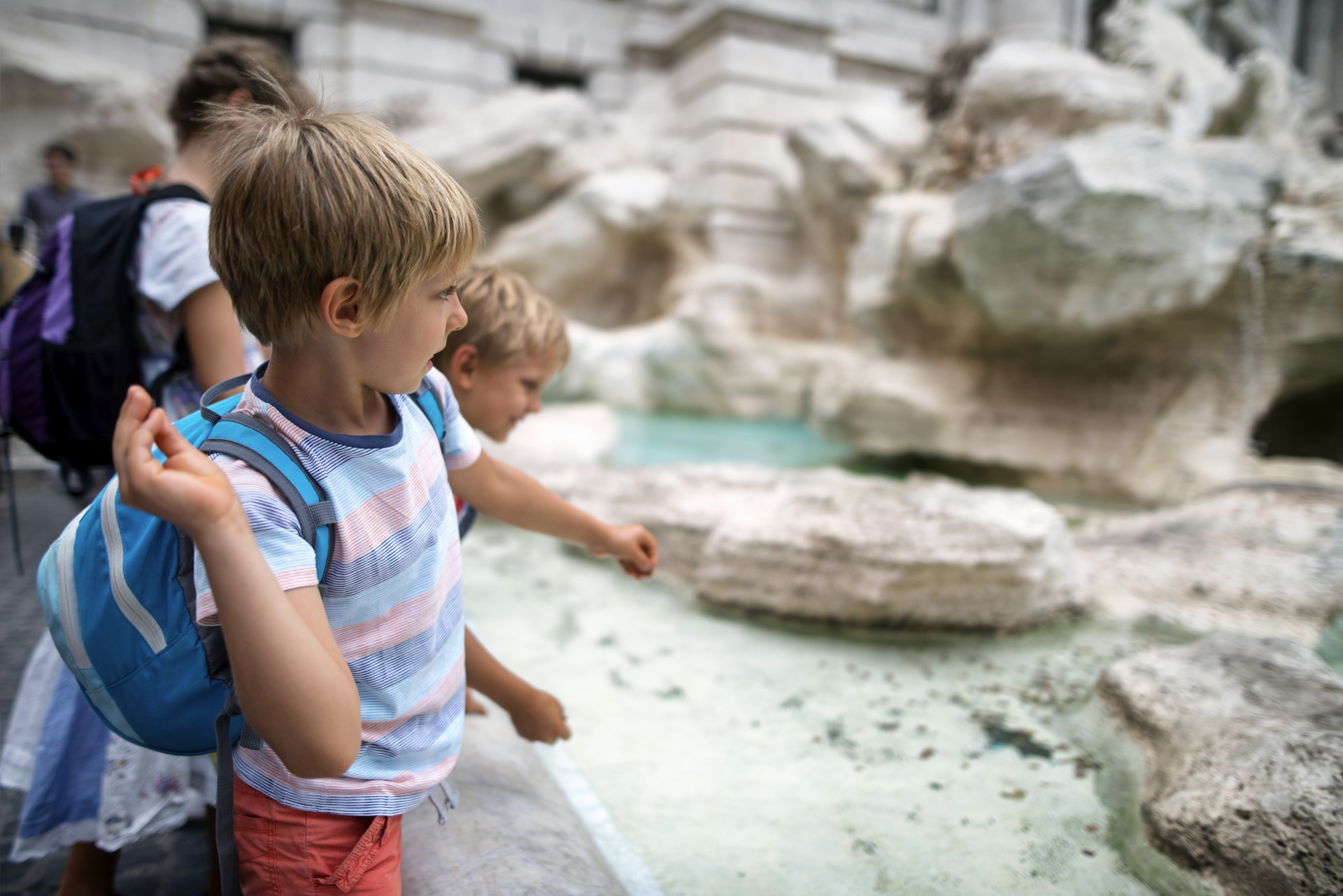 Kids tourists throwing coins into Trevi Fountain, Rome
