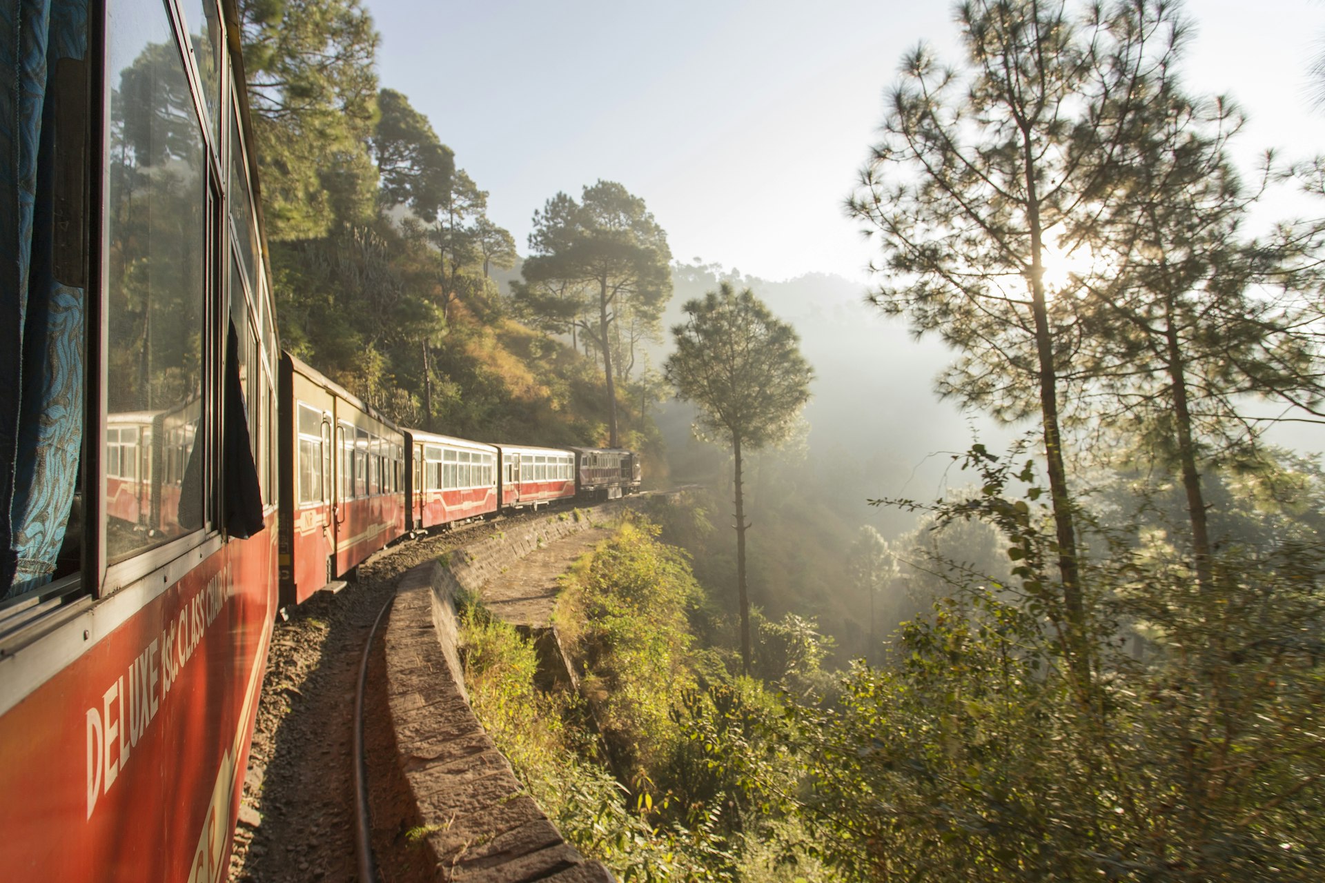 The Shivalik Deluxe Express train from Kalka to Shimla rounds a corner its journey. The train line is very scenic, hugging the side of a mountain and surrounded by forest.