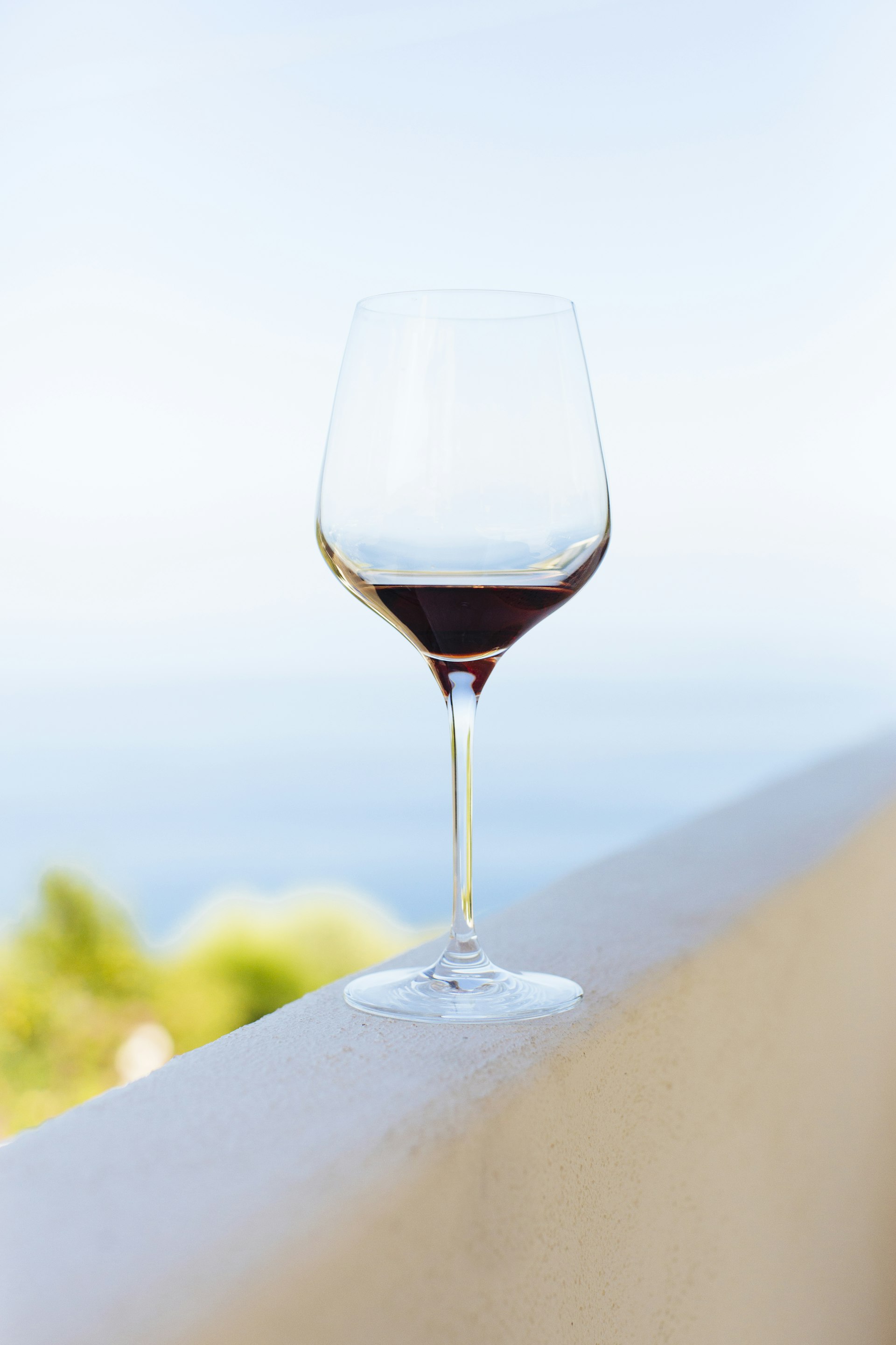 A glass of wine with a bit of wine at the bottom rests on a concrete ledge