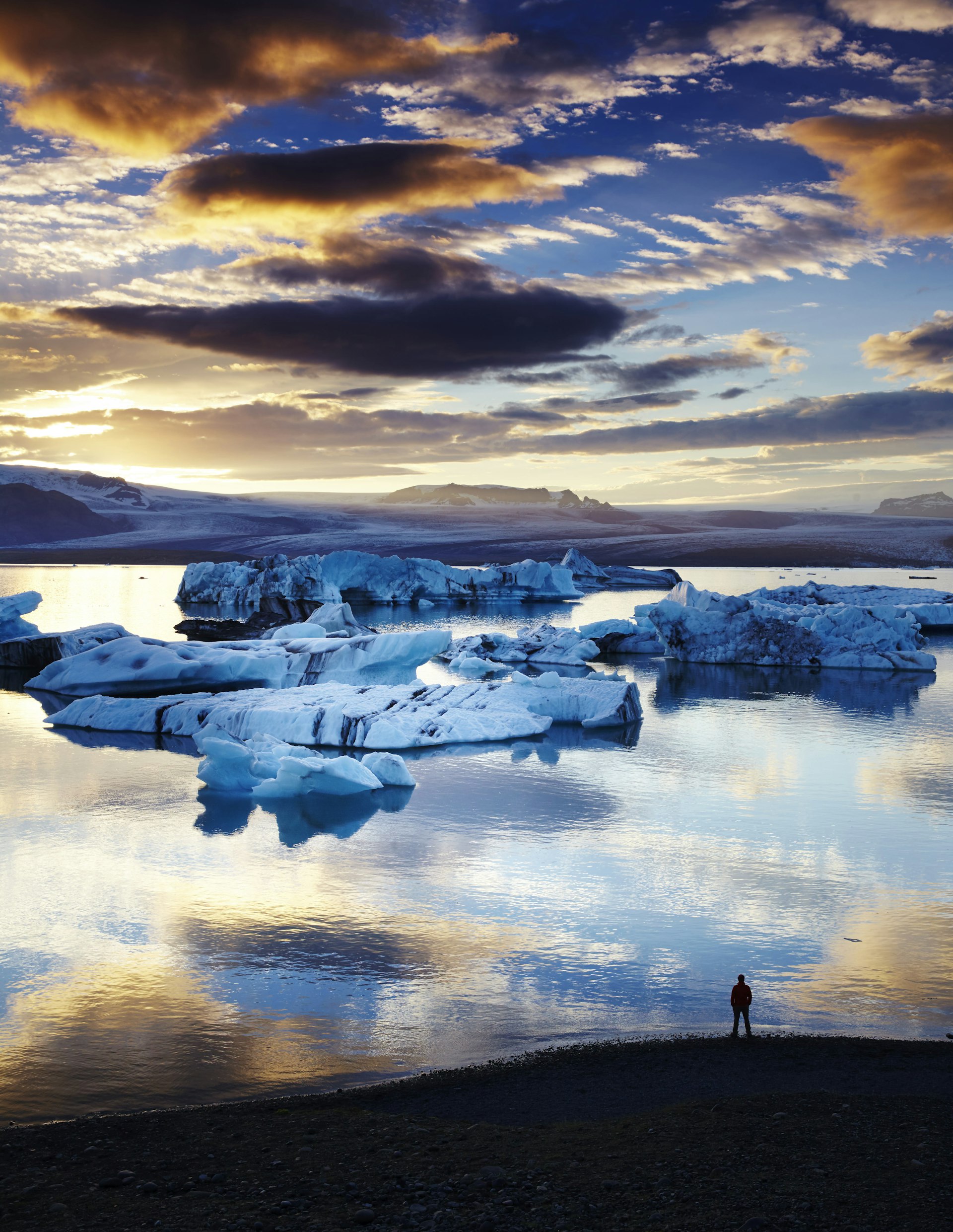 The sun sets over a waterway dotted with large blocks of ice, given a sense of perspective only by the single person silhouetted on the beach