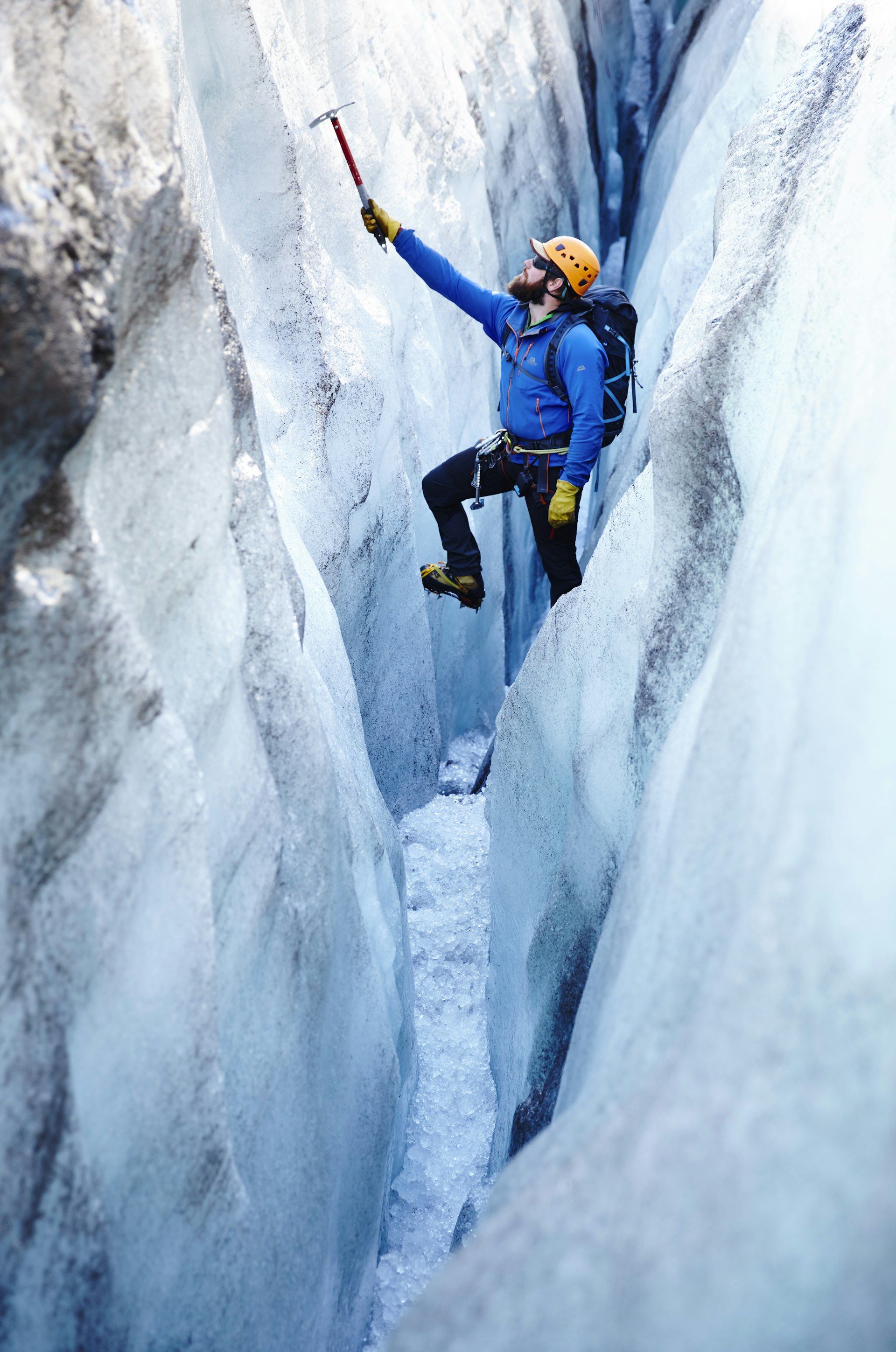A man in climbing gear hangs off an ice-pick in an icy crevasse