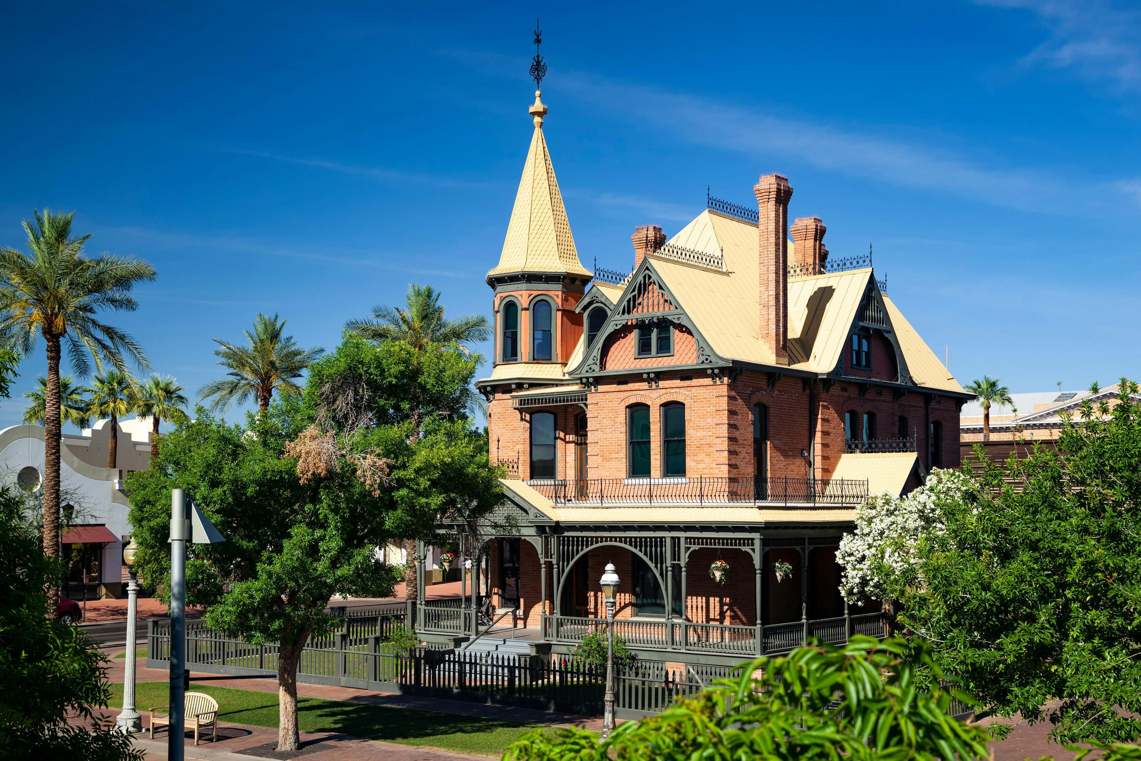 The turrets and yellow roof of the Victorian-style Rosson House Museum on Heritage Square Park, Phoenix, Arizona in the USA peep through green trees on a clear afternoon