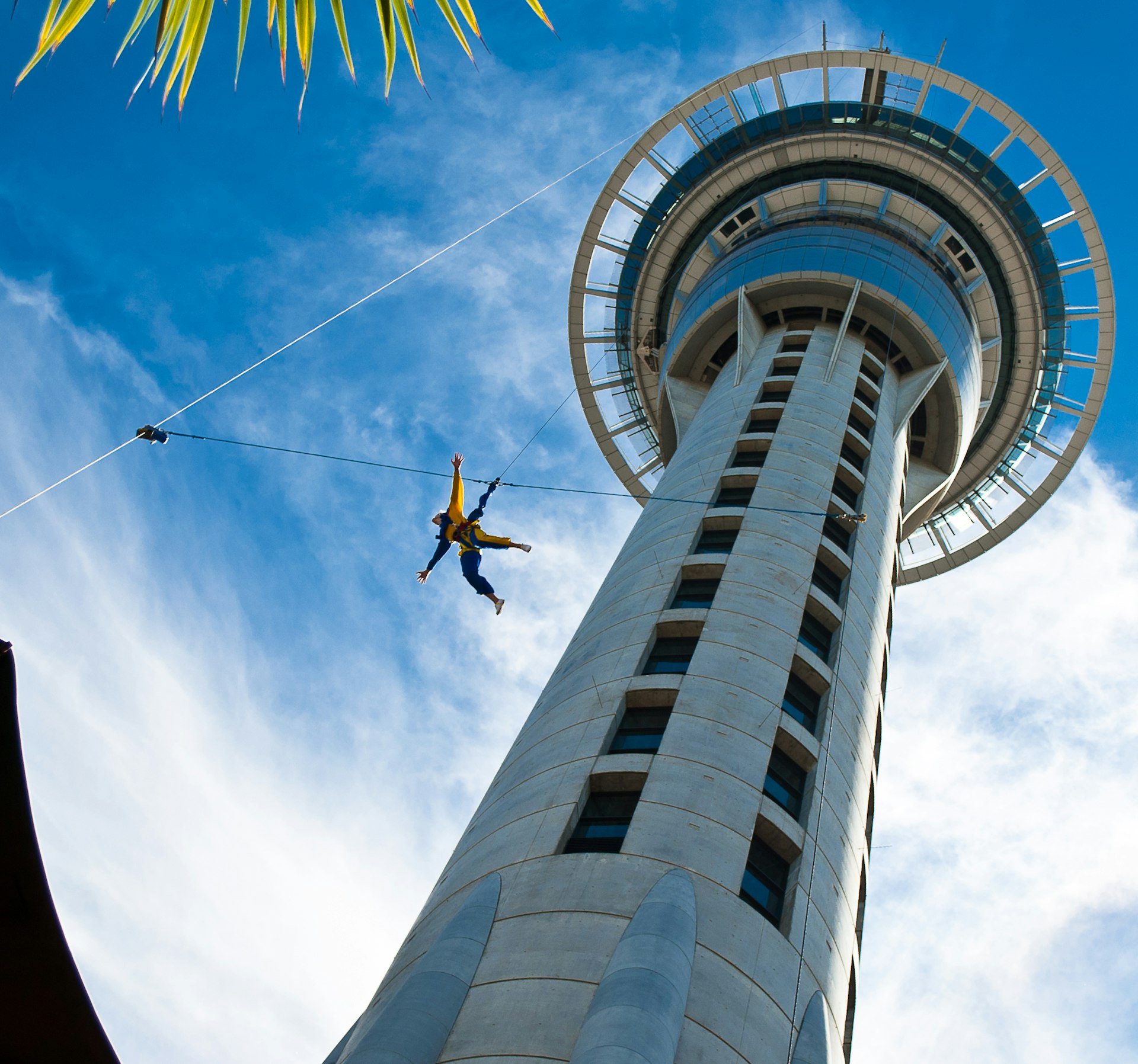 Auckland Sky Tower seen from below against a blue sky, with someone jumping off