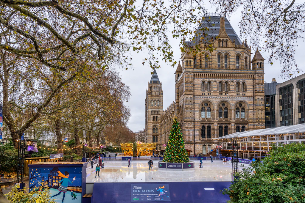 An ice rink with a Christmas tree centerpiece outside a huge Gothic style brick building