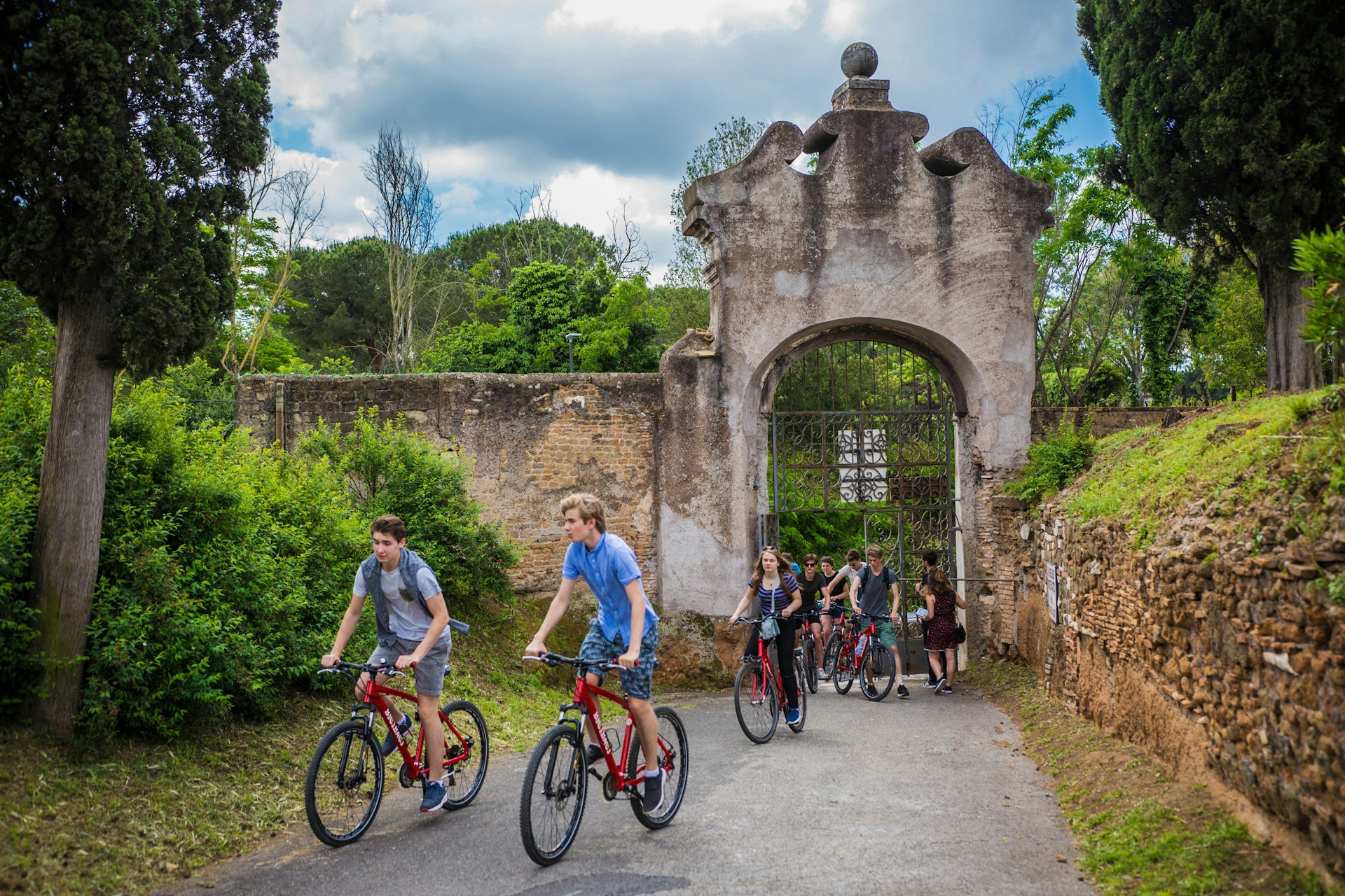 A group of kids bike through the entrance to the catacombs in Rome