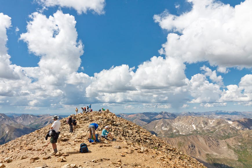 A group of hikers at the top of a mountain in Colorado looking out over other peaks on a sunny day