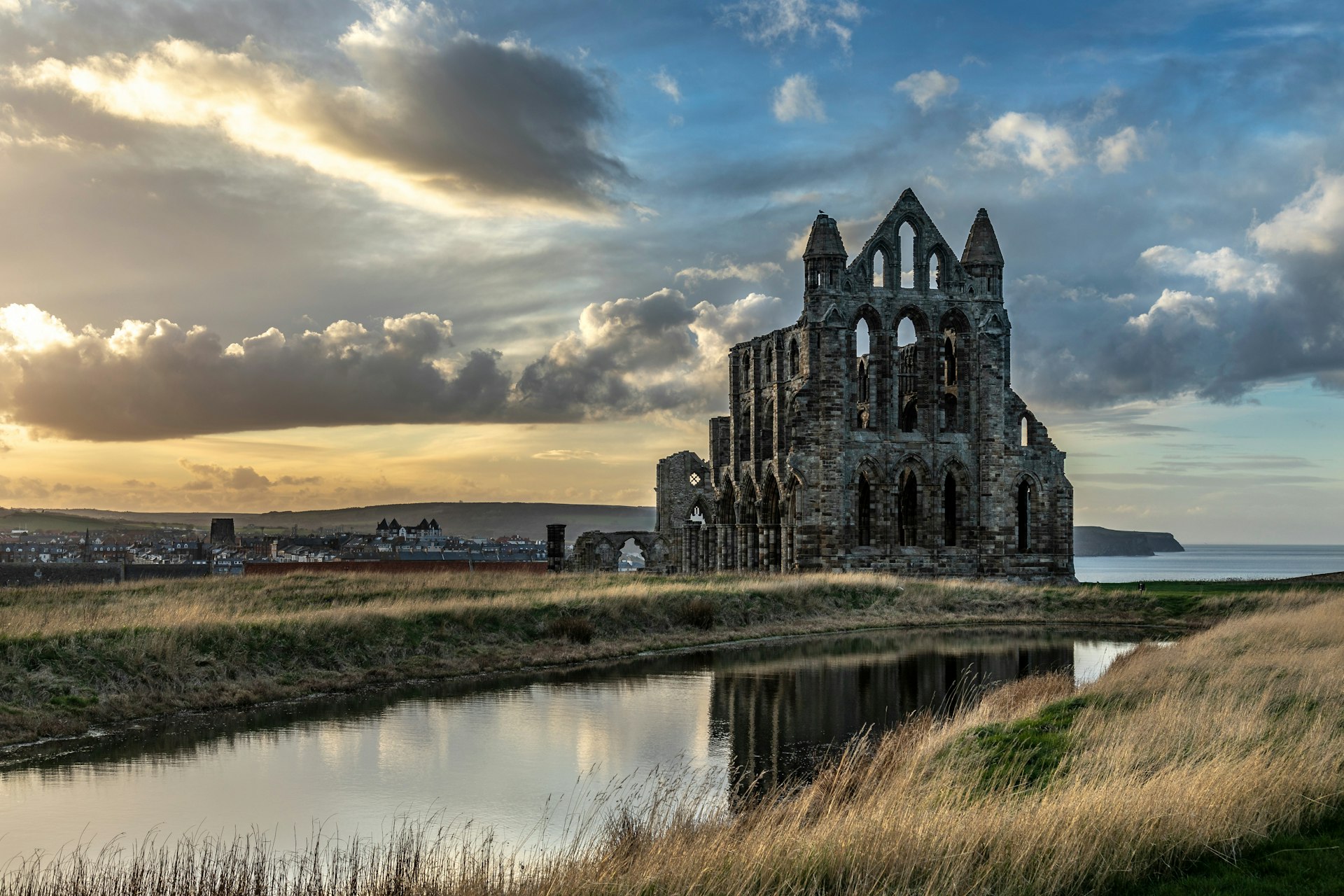 A ruined abbey building on a cliff, fronted by long grass meadows and backed by the sea