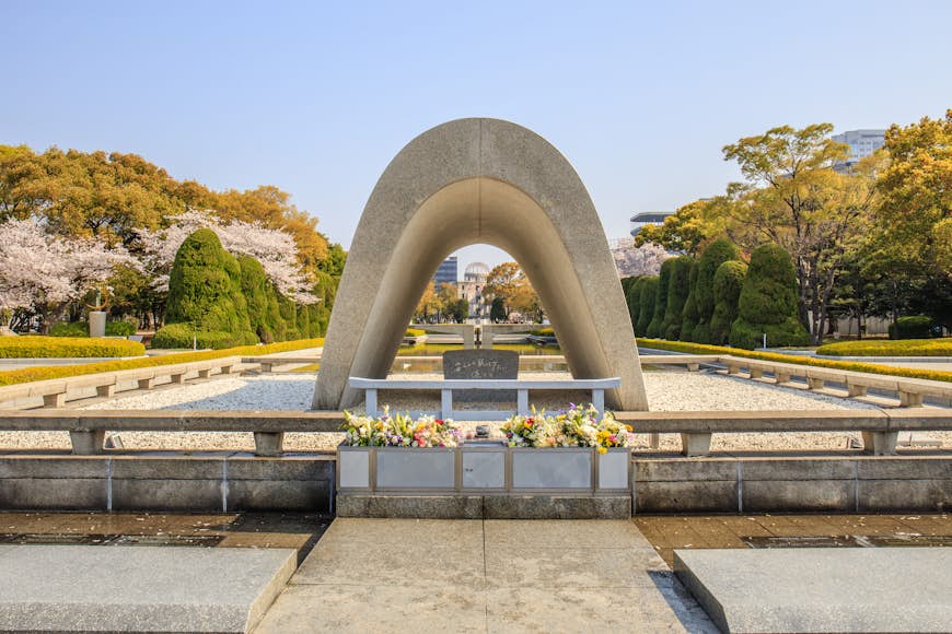 Memorial Cenotaph i Hiroshima Peace Memorial Park.  Cenotafen är ett vitt, slätt monument i halvoval form.