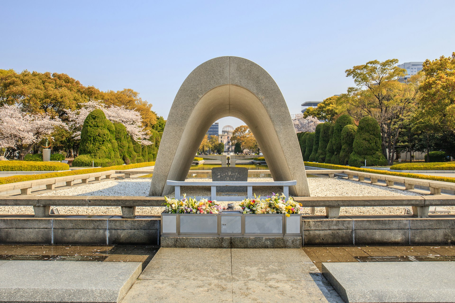 The Memorial Cenotaph at Hiroshima Peace Memorial Park. The cenotaph is a white, smooth monument in a half oval shape.