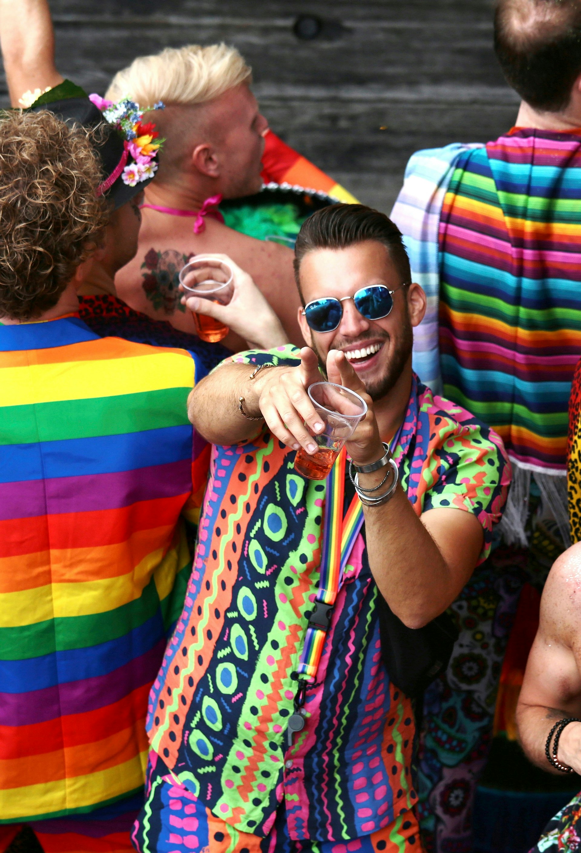 Revellers wearing rainbow colors celebrating Pride. One in glasses is smiling and posing for the camera