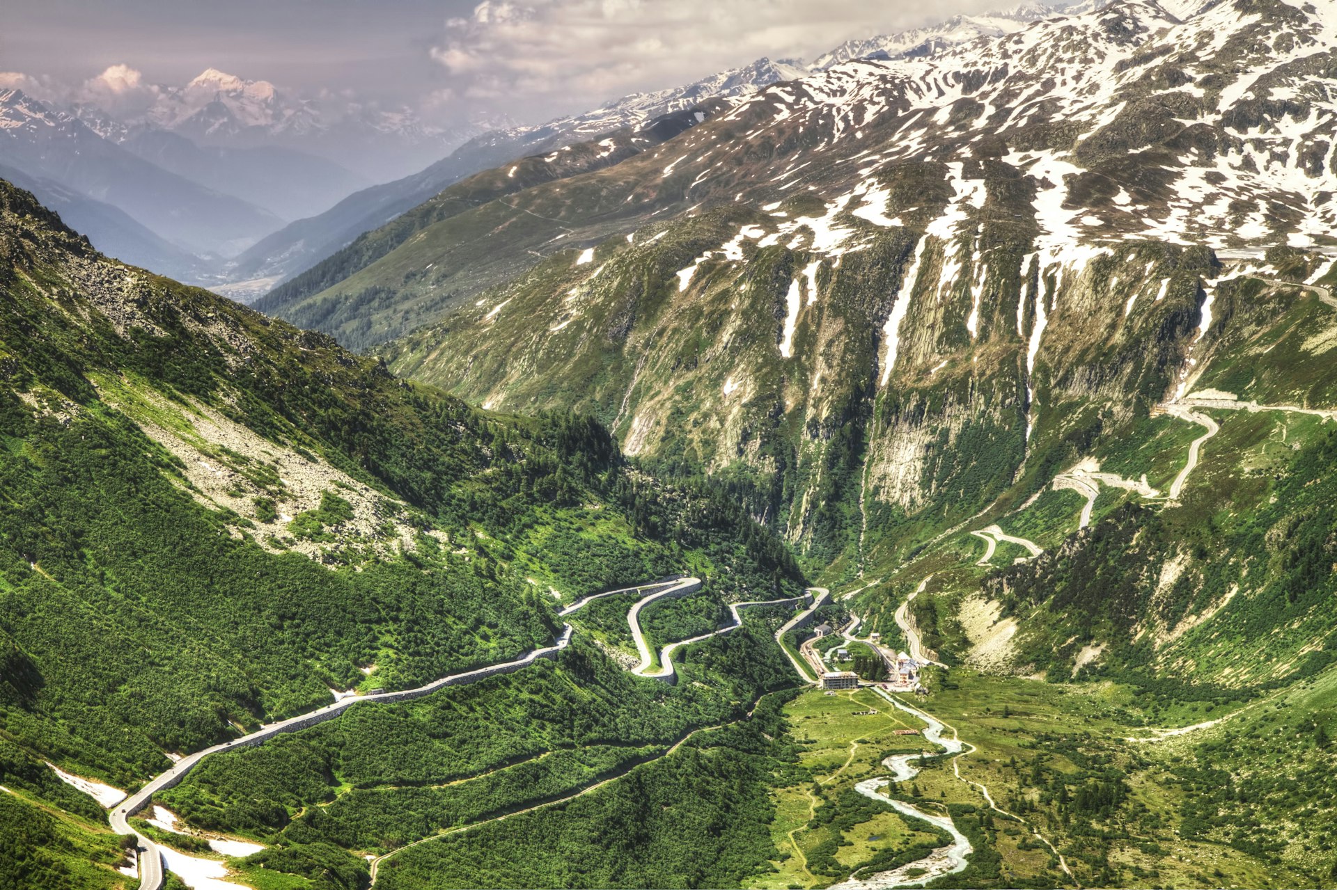 A lone road through the Furka Pass wiggles through a valley that is hemmed in by giant, snow-capped mountains in Switzerland