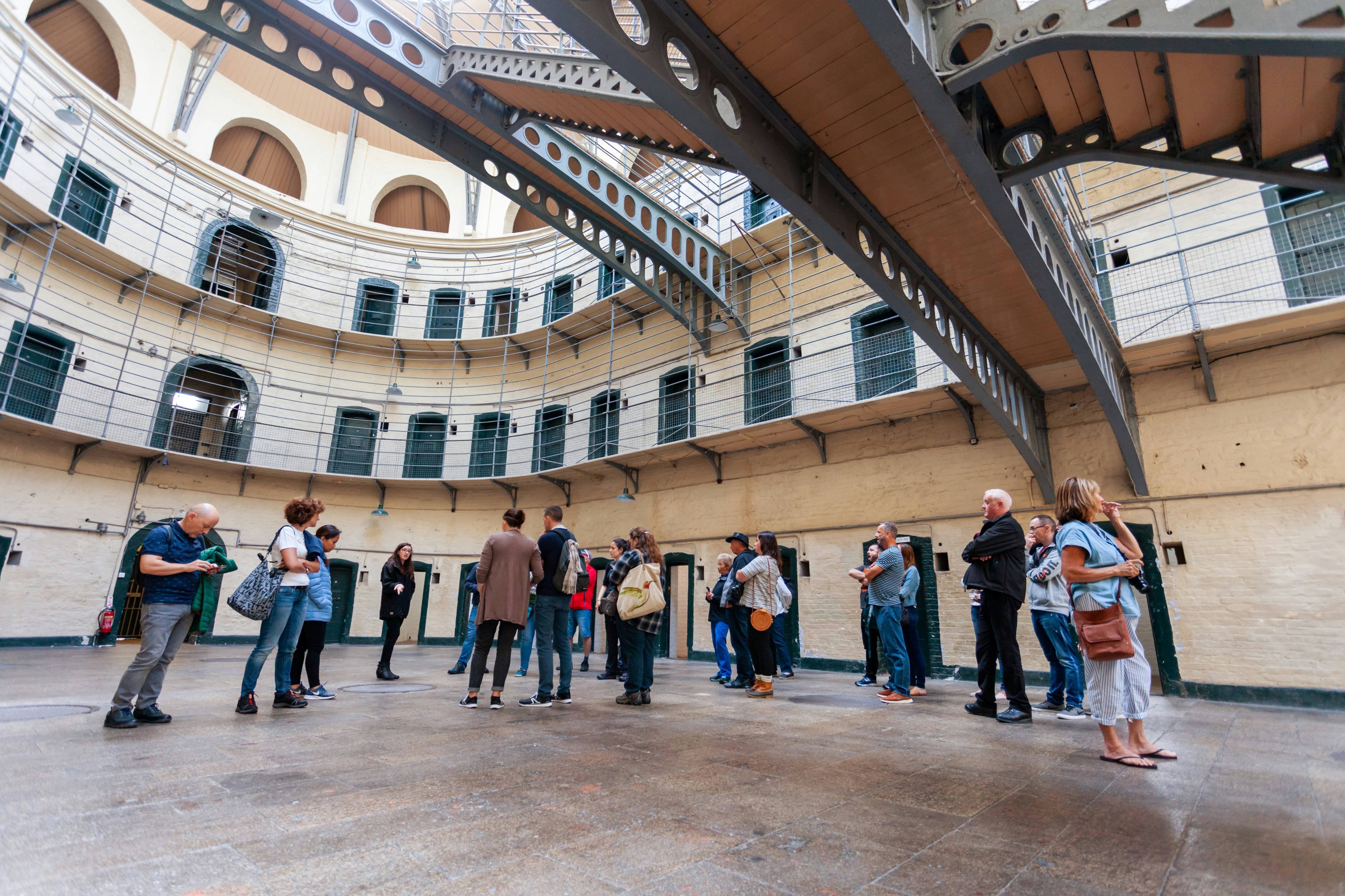 A tour group stands in the big hall of a prison building surrounded by doors to individual cells