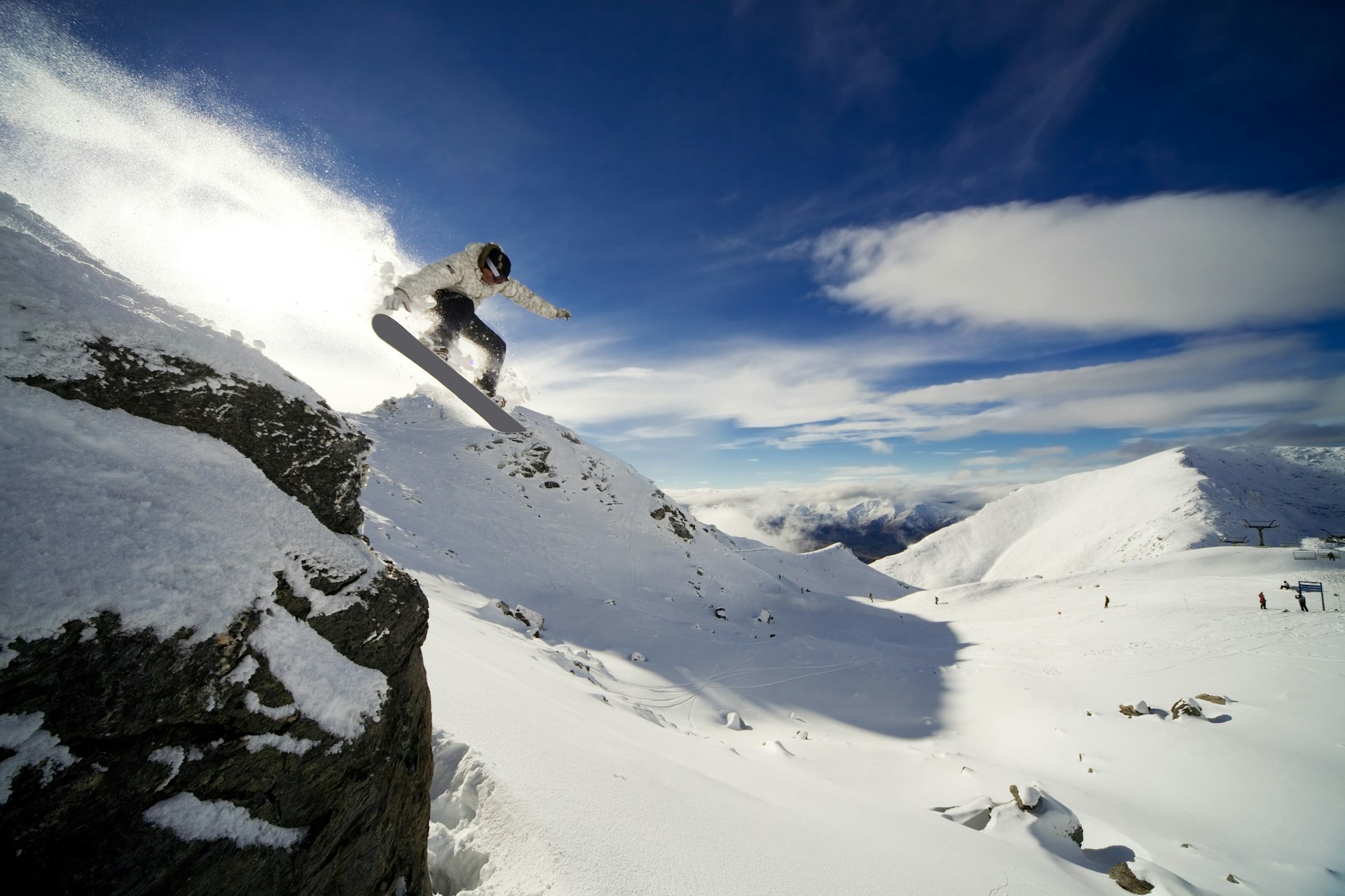 A snowboarder jumping off a cliff on a sunny day