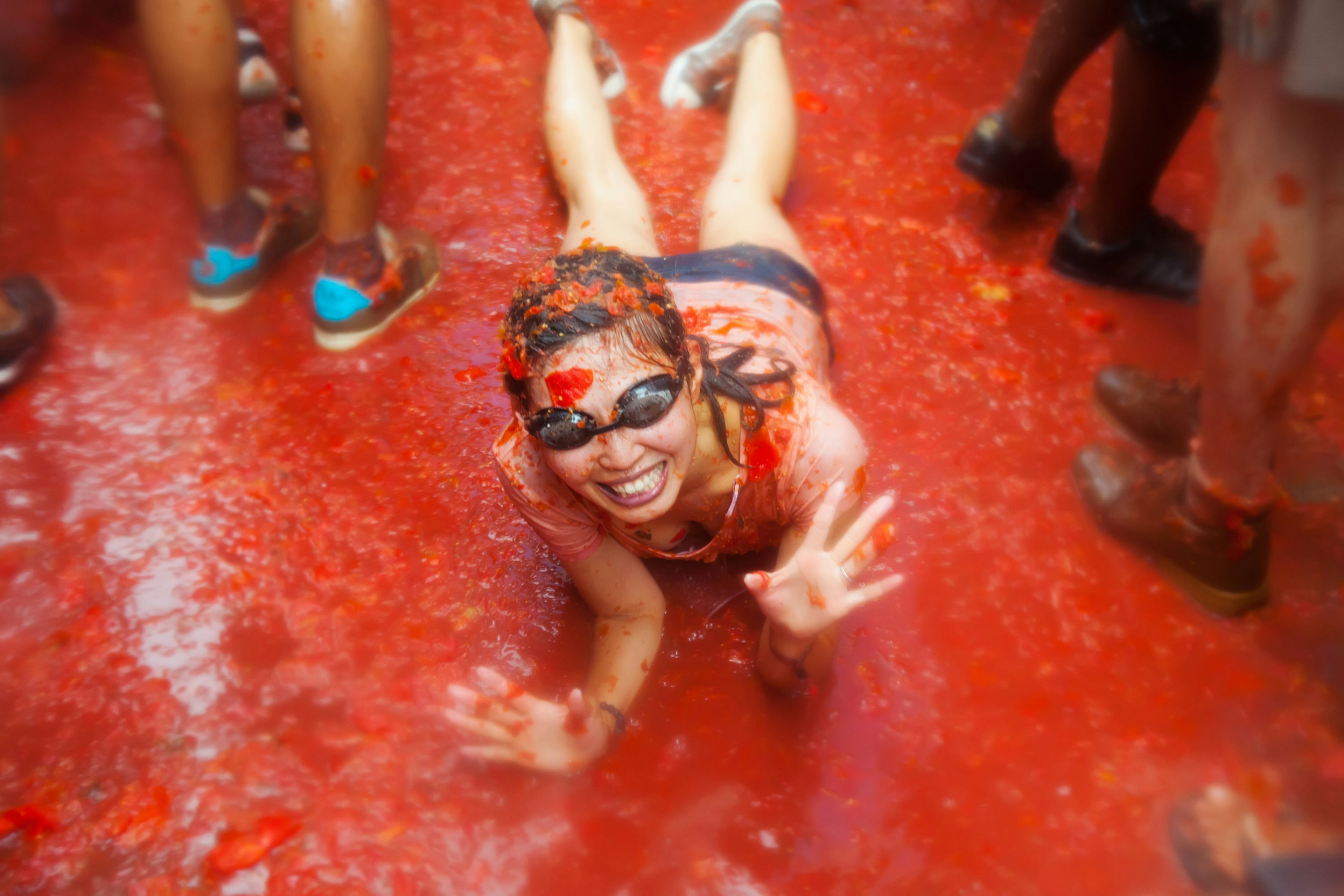 Girl lying in tomato juice on the ground at La Tomatina festival, where people fight with tomatoes in the street.