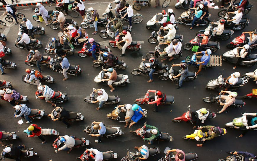 A top-down view of a very busy road during rush hour in Ho Chi Minh City. The road is filled with people on scooters, most of them have at least two people on each bike.