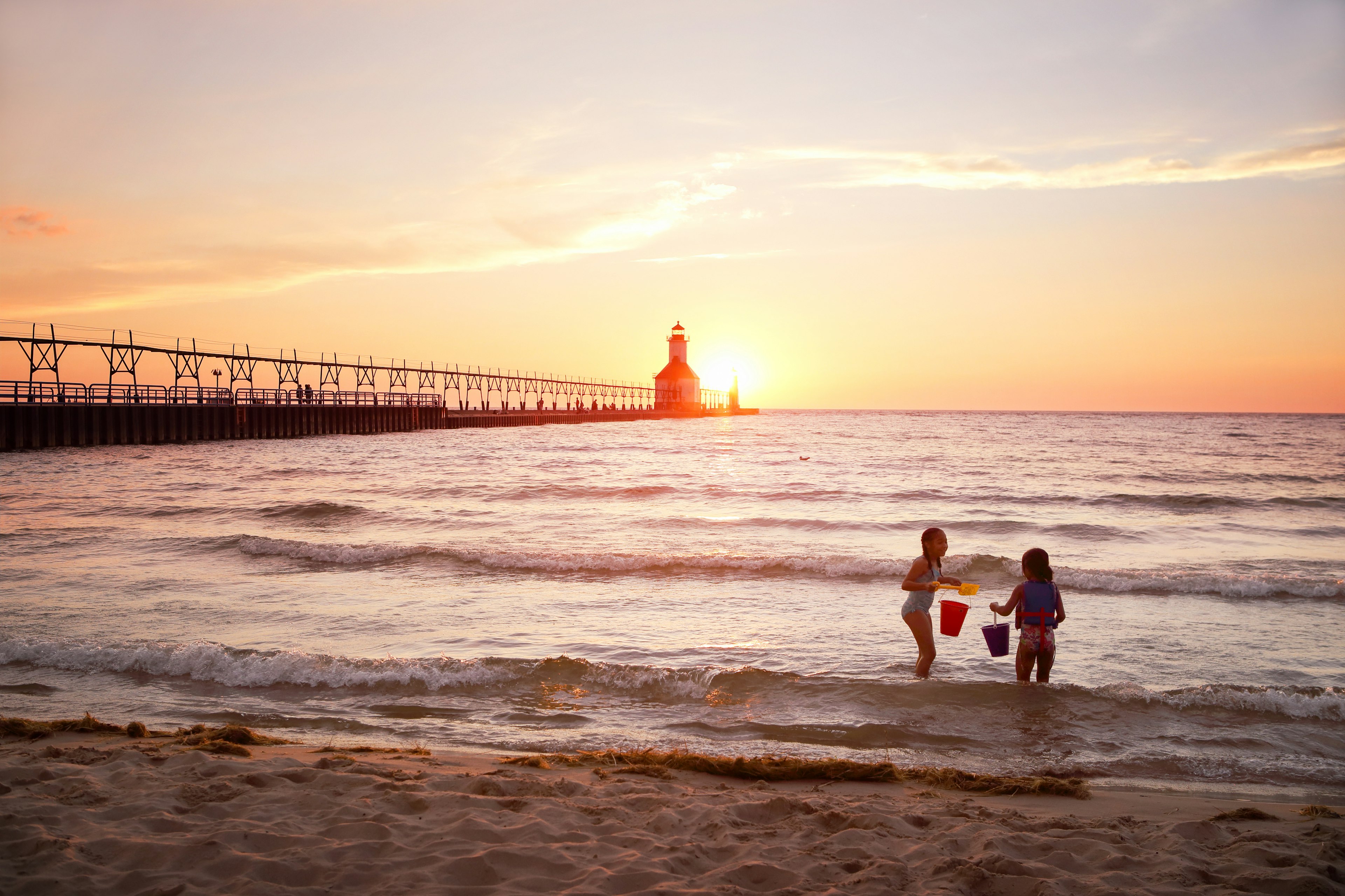 Kids playing in the water in front of St Joseph Lighthouse on Lake Michigan during sunset.