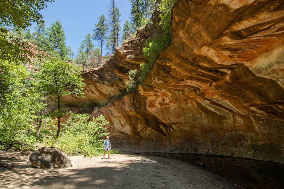 Man trekking through Oak Creek Canyon on the West Fork trail in Arizona, between Flagstaff and Sedona surrounded by beautiful red rock and lush green forest