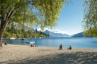 February 15, 2012: Visitors relax on the shore of Lake Wakatipu in Queenstown.