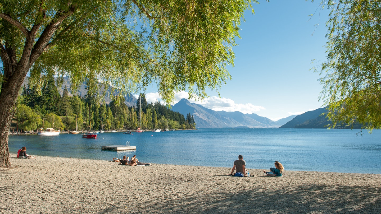 February 15, 2012: Visitors relax on the shore of Lake Wakatipu in Queenstown.