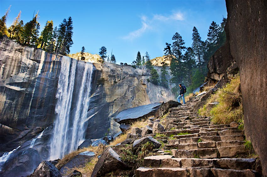 站立在石步和敬佩在优胜美地国家公园的一个男性远足者瀑布。