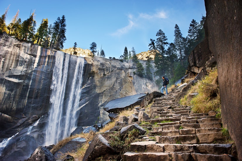 A male hiker standing on stone steps and admiring a waterfall in Yosemite National Park.