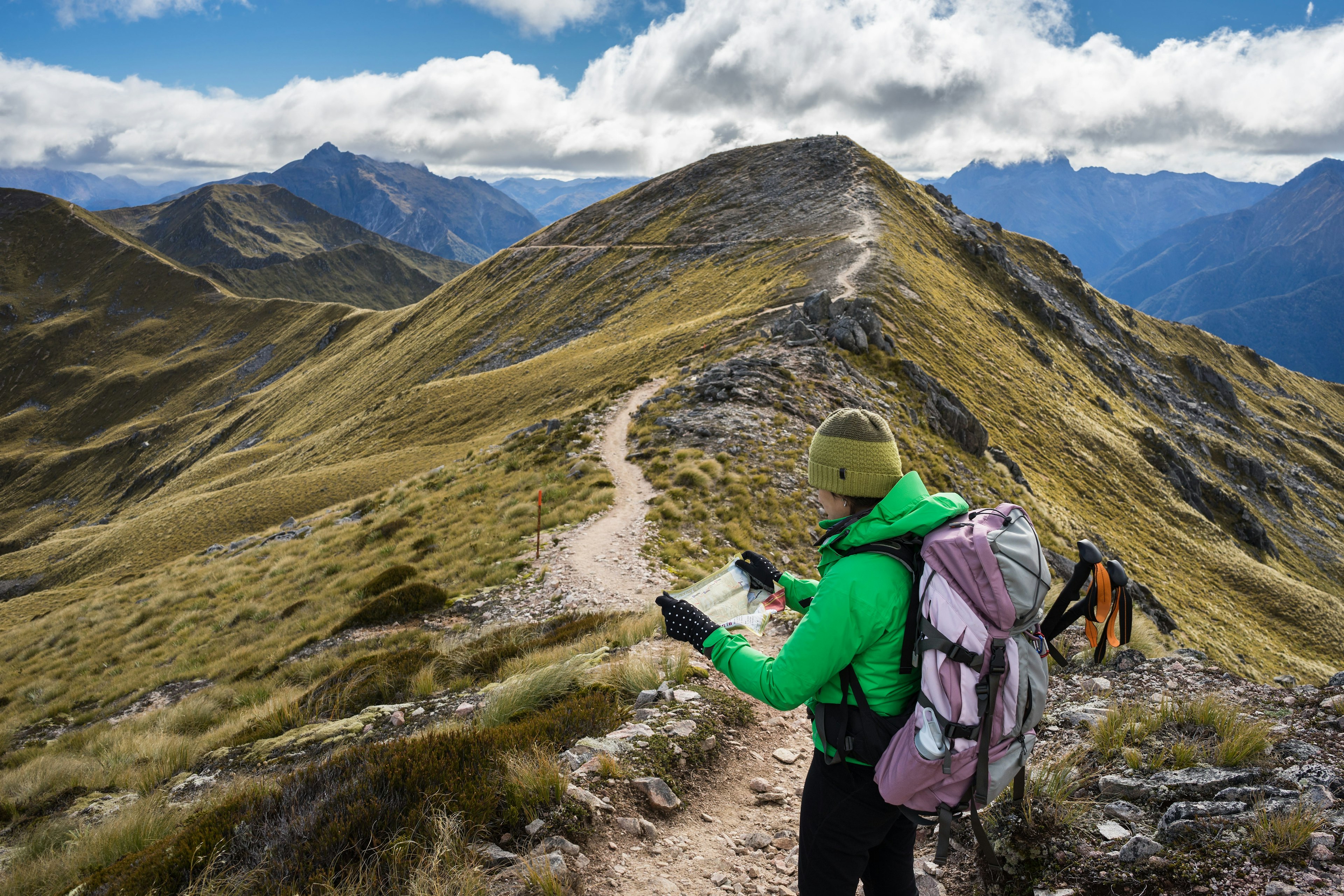 Female hiker looking at a map on a mountainous section of a hiking trail.