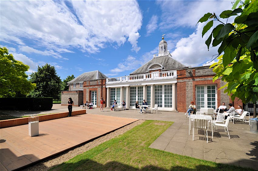 The Serpentine Gallery, Hyde Park A single-story brick building with white columns outside it and a small pagoda on its pointed roof.
