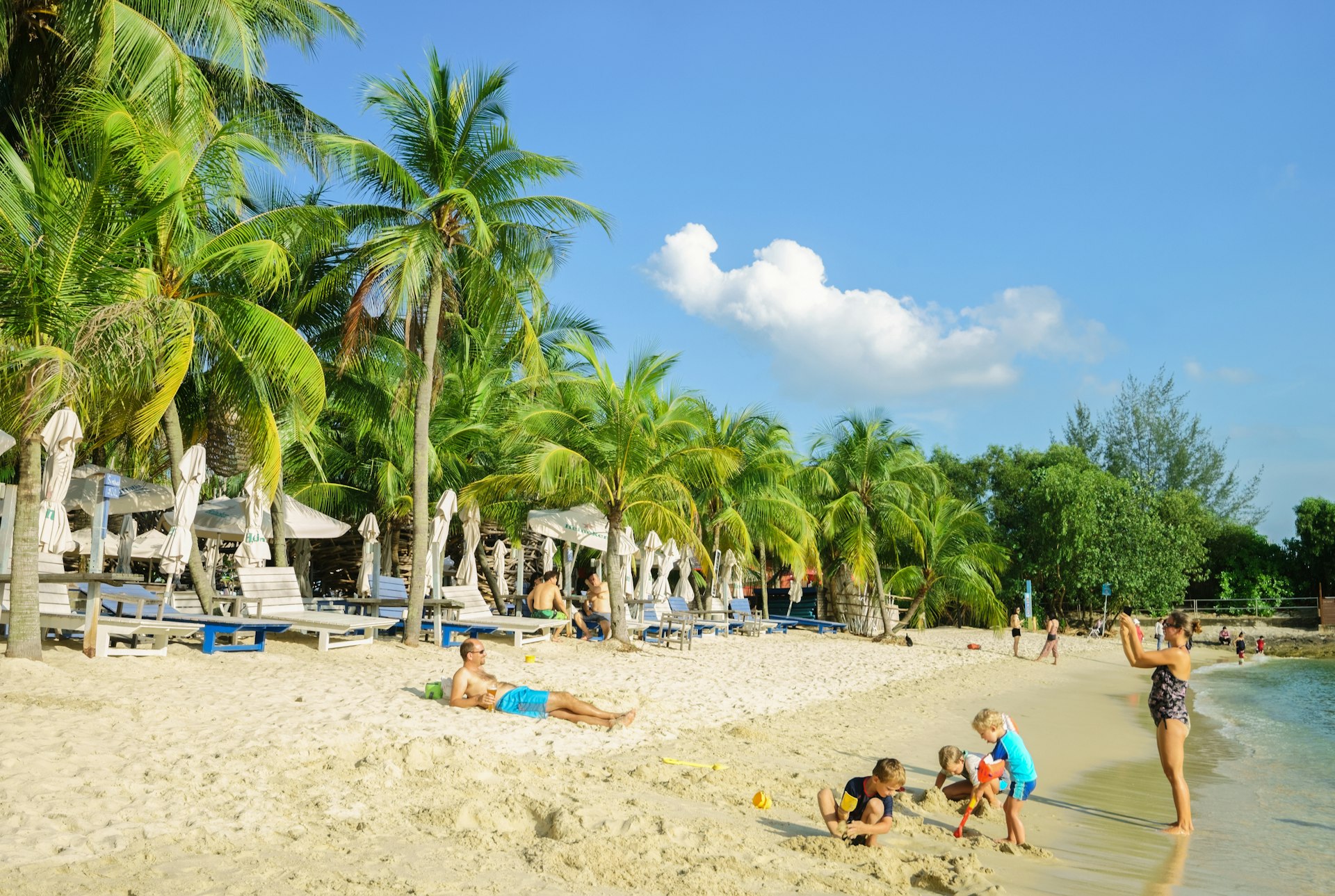 Families on the sandy palm-lined beach at Sentosa Island 