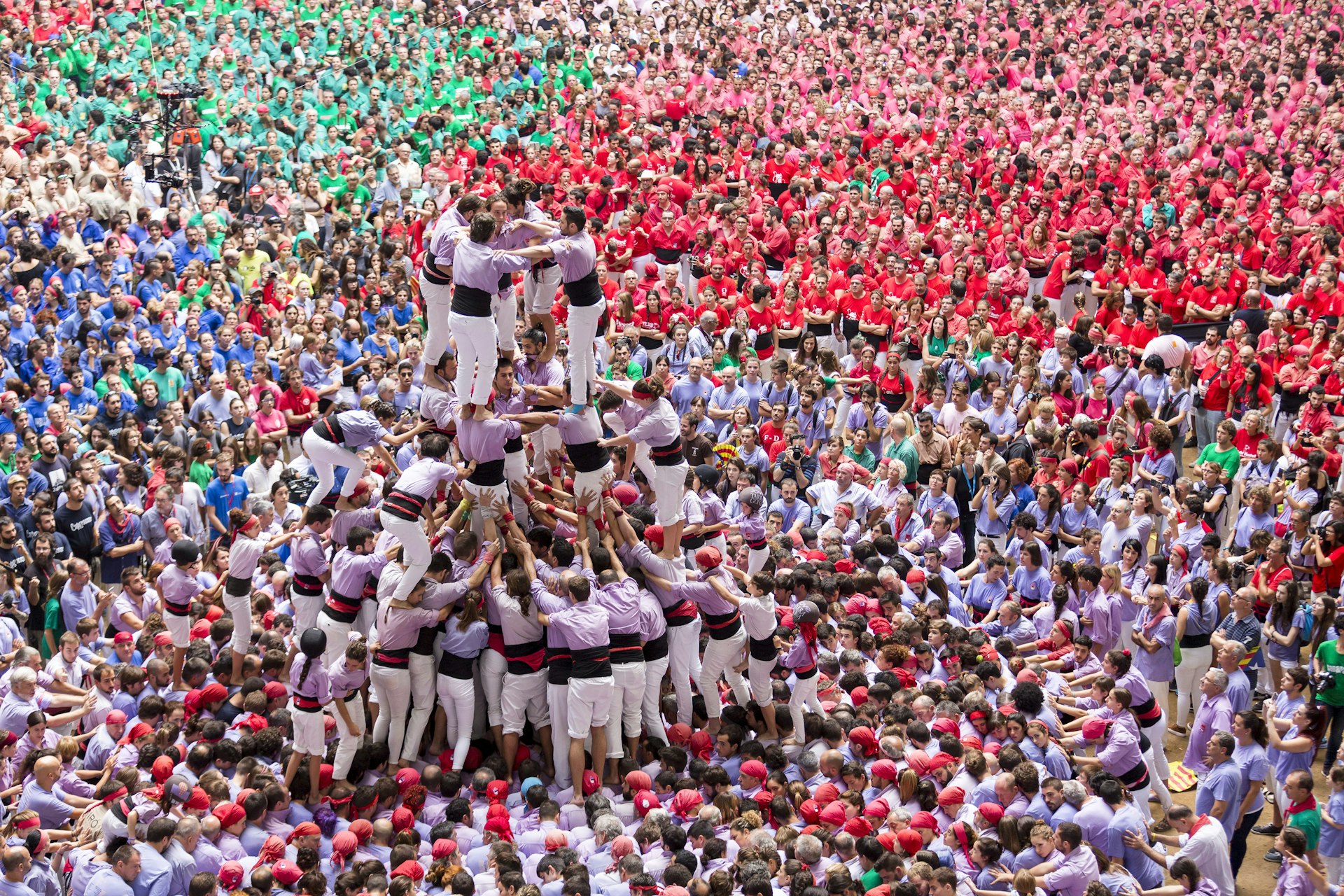 A huge tightly packed crowd shot from above. A tower of people standing on each other's shoulders is the focal point