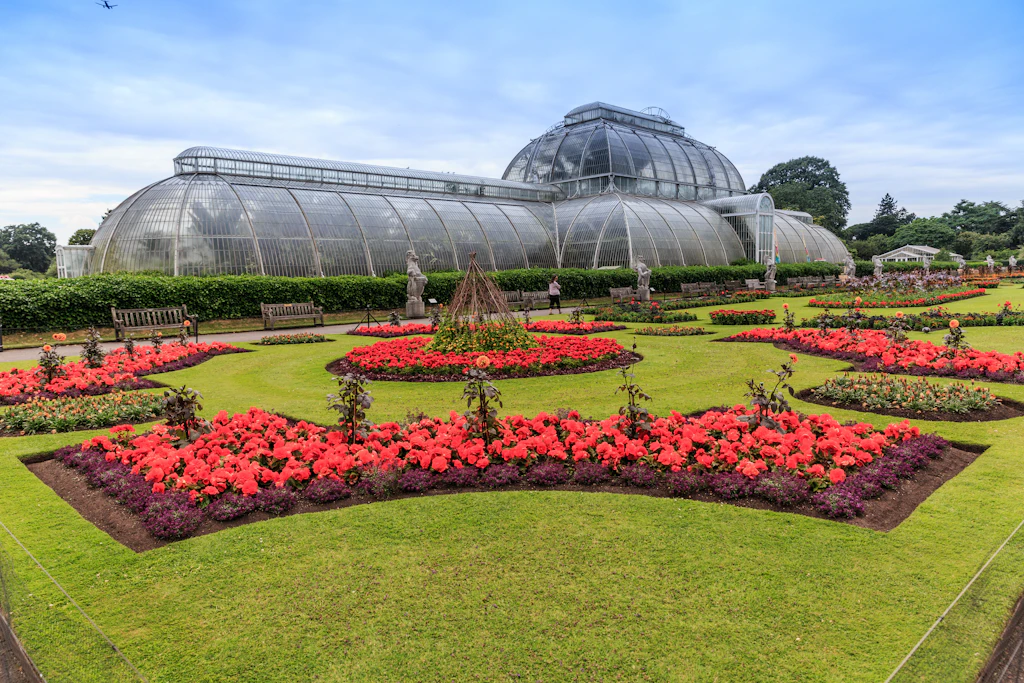 A huge glasshouse in manicured gardens with pink flowers in flowerbeds 