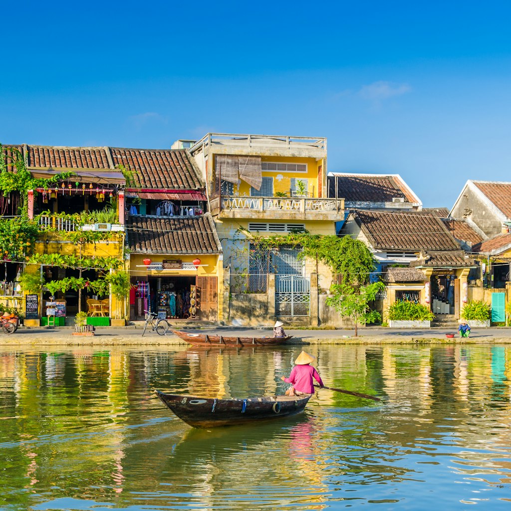 A traditional boat paddles past riverside houses in Hoi An.