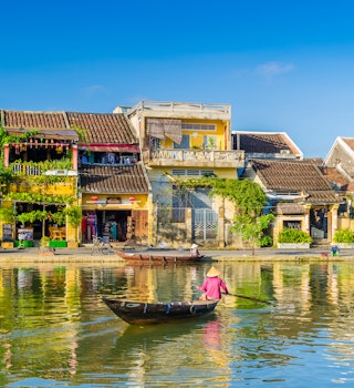 A traditional boat paddles past riverside houses in Hoi An.