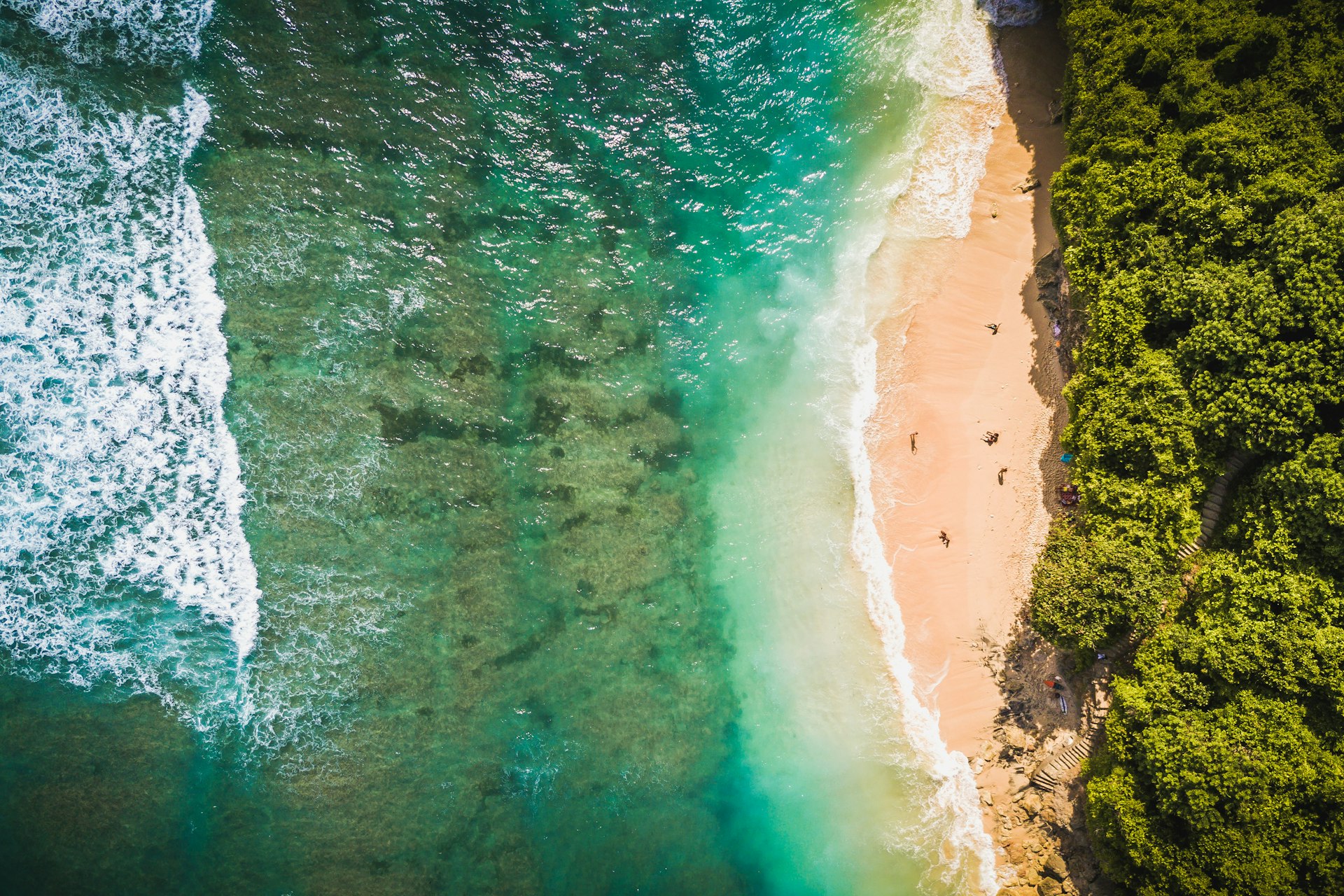 Aerial view of Green Bowl Beach with a green sea and sand surrounded on all sides by greenery in Bali, Indonesia