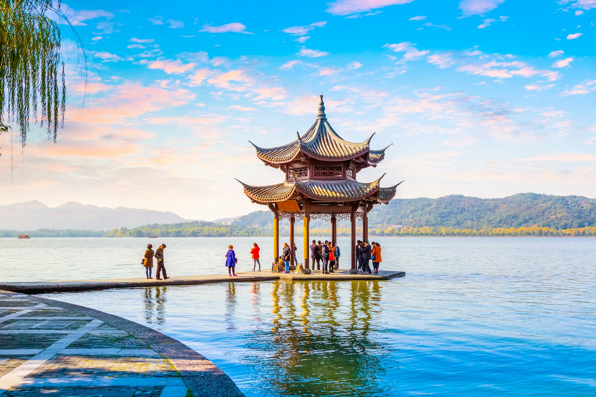 A pagoda stands on a clear lake. There are people underneath it and the sky is a clear blue.