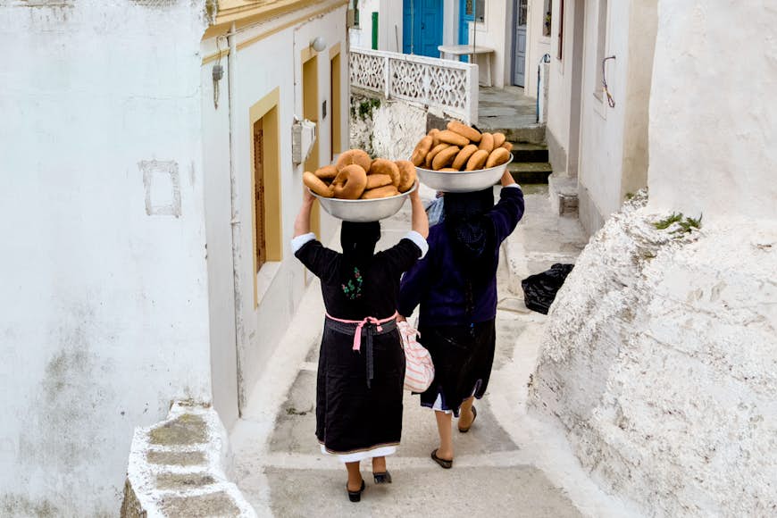 Women carry bowls of bread for Greek Orthodox Easter celebrations down a narrow lane in Olympos on Karpathos Island, Greece