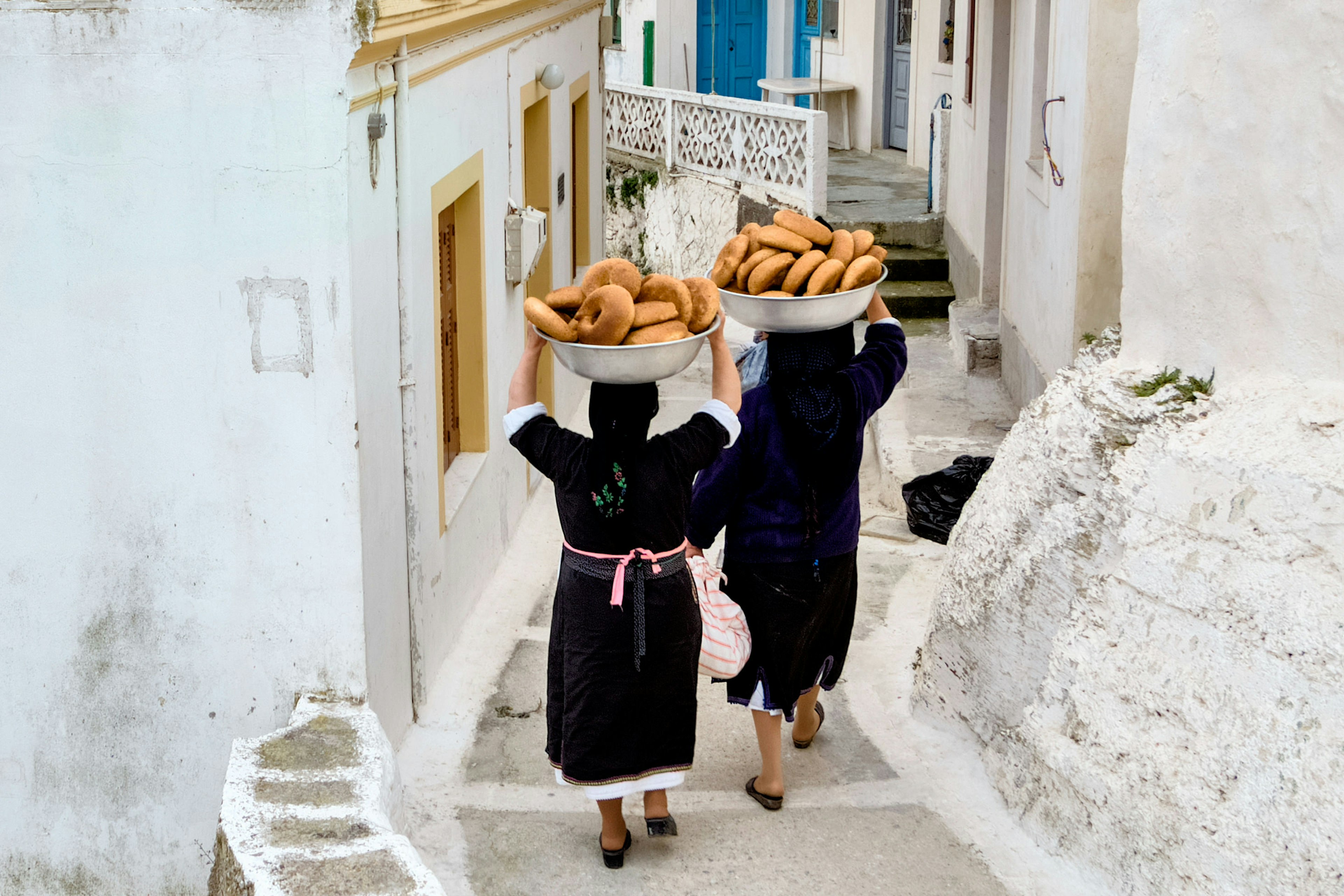 Women carry bowls of bread for Greek Orthodox Easter celebrations down a narrow lane in Olympos on Karpathos Island, Greece