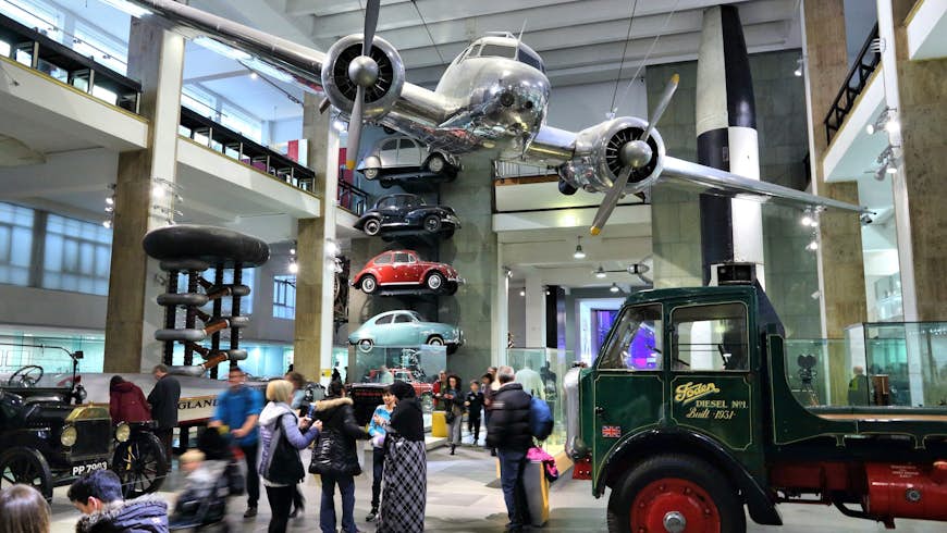 A small plane is suspended from the ceiling of a vast museum room packed with different forms of transport
