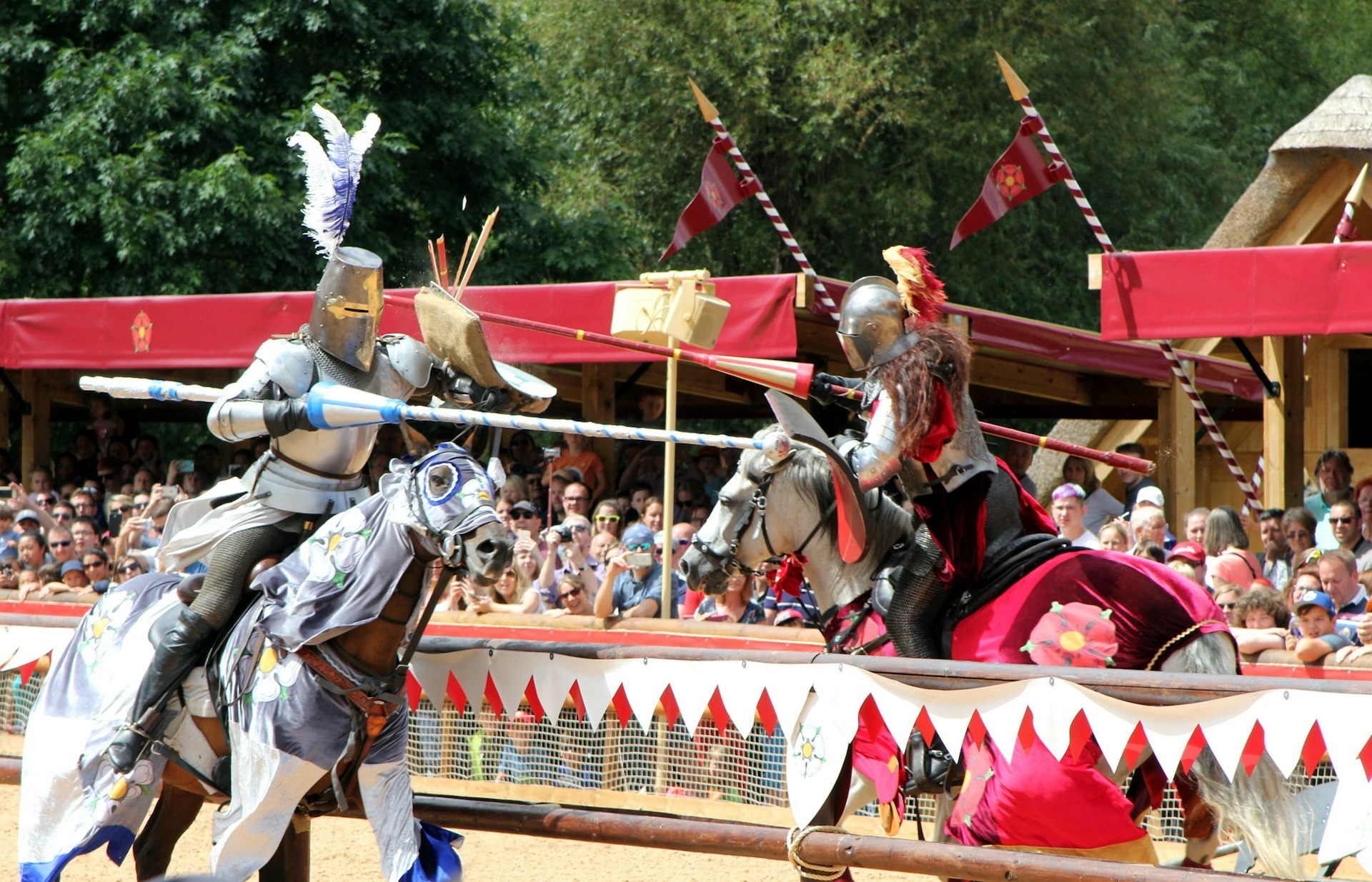 Dos caballeros a caballo con armadura se acercan con garrotes en una recreación de batalla con una multitud de espectadores